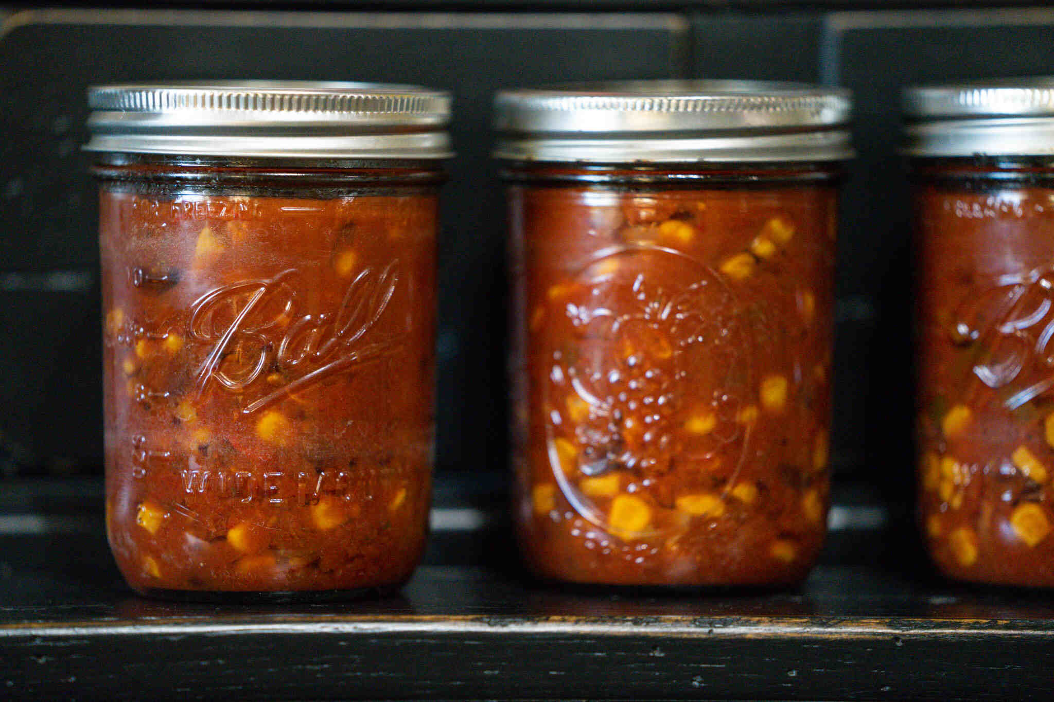 Two pint canning jars with black bean and corn salsa in them. Sitting on black cabinet